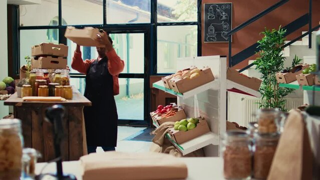 Storekeeper arranging crates of fruits and veggies on shelves, organizing freshly harvested produce at local supermarket. Woman merchant preparing store goods for customers. Handheld shot.