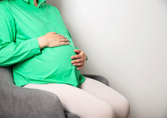A pregnant girl in a green blouse sits on a chair and counts regular contractions before the onset...