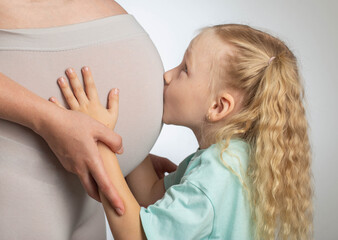 A little girl kisses the belly of her pregnant mother. The concept of motherhood and love for...