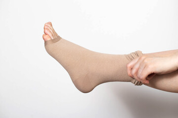 A woman puts on compression stockings for legs with varicose veins. Pain and swelling in the legs,...