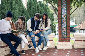 Fototapeta premium group of four college friends relaxing with book and smartphone