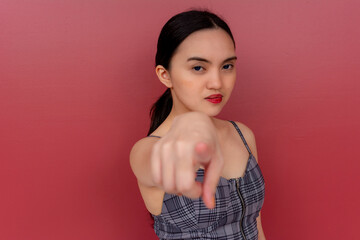 A displeased young asian woman calling out someone, gesturing with her finger. Isolated on a red...