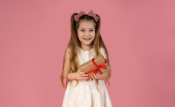 The little girl is very happy to have received an unexpected gift, and she is pictured enjoying this gift on a pink background. The girl has a very beautiful smile.