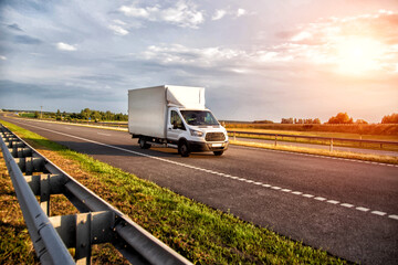 A white light-duty van isotherm transports products between cities on a country road in summer, sunset, industry