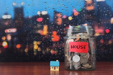 Real estate, property investment, saving money for house concept. Glass jar full of coins and miniature house with copy space for text