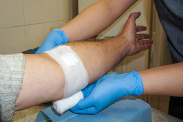 Doctor bandaging his patient hand in medical office.