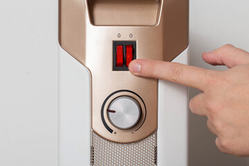 A man's hand turns on an electric heater, close-up.