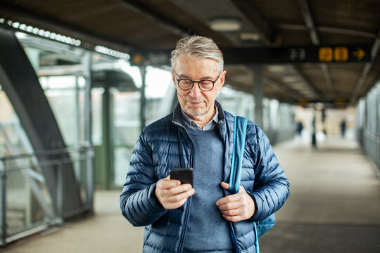 Traveling senior man using smartphone at train station