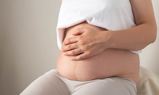 A pregnant girl sits with a bare belly in the office of a cosmetologist and massage therapist. Concept of skin care on the abdomen during pregnancy. Skin changes and stretch marks 