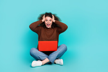 Full size photo of pretty young girl sit floor netbook shocked reaction wear trendy brown outfit isolated on cyan color background