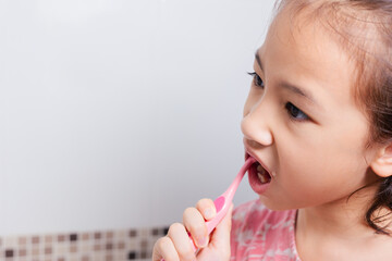 Close up face and mouth of Adorable little Asian girl enjoys her morning routine in relaxed expression for brushing her teeth in clean and bright bathroom for healthy dental care of kid and child.