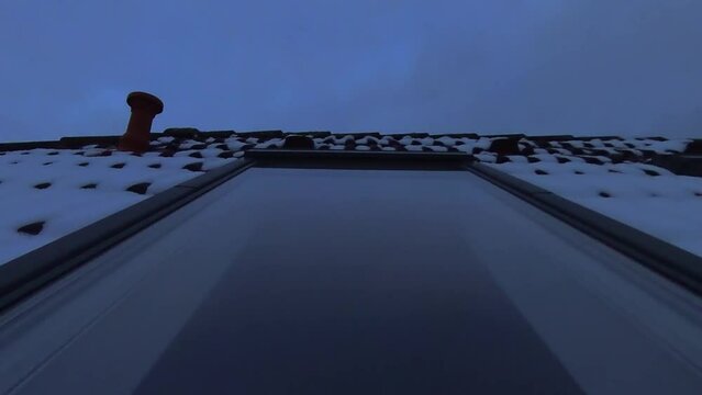 Dachfenster in verschneitem Dach mit sich spiegelnden Wolken die Abends im Zeitraffer vorbeiziehen, rote Ziegel, Dachd&auml;mmung