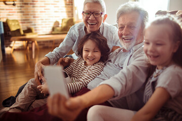 Happy grandparents taking selfie with grandchildren at home