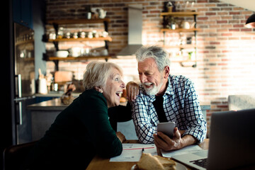 Senior couple doing home financials in the kitchen with laptop