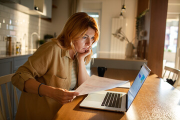 Concerned woman reviewing documents while working from her home kitchen