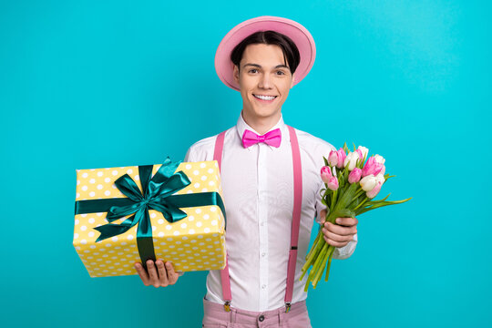 Portrait of cheerful positive man dressed pink cap bow tie hold bouquet give you present on new year isolated on blue color background