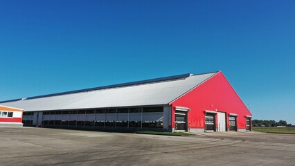 The barn is red in color. A building for keeping cows in winter in the cold season. Where cattle live on a dairy farm in winter. Red huge shed for animals. Red facade of a building made of metal struc © Aerial Drone Master