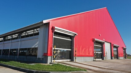 The barn is red in color. A building for keeping cows in winter in the cold season. Where cattle live on a dairy farm in winter. Red huge shed for animals. Red facade of a building made of metal struc