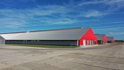 Huge long sheds with red facade made of metal structures with triangular metal roof for keeping...