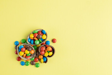 Top view of scattered multi-colored candies in broken Chocolate Easter eggs on yellow background, Happy Easter Concept, copy space