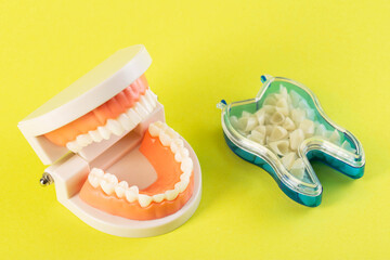 Dental crowns in the shape of a tooth on a yellow background and a medical model of a dental jaw. The concept of manufacturing ceramic hypoallergenic crowns for dental prosthetics in orthodontics. 