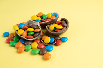 Scattered multi-colored candies in broken Chocolate Easter eggs on yellow background, Happy Easter Concept