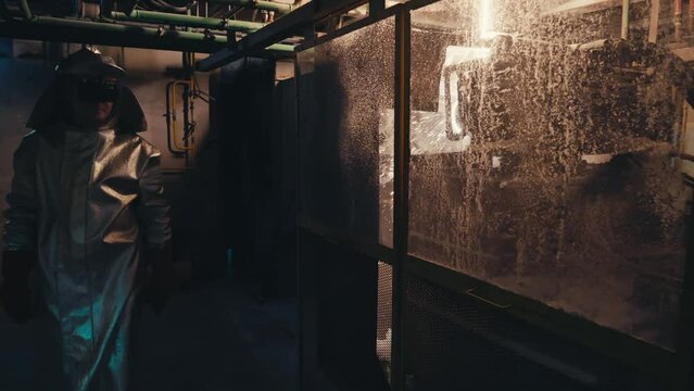 Thermal Insulation Materials Manufacturing. Asbestos Cardboard Production. Inside a Dark Workshop. Male Factory Worker Wearing a Shiny Fireproof Coat and Protective Goggles is Walking Out workshop