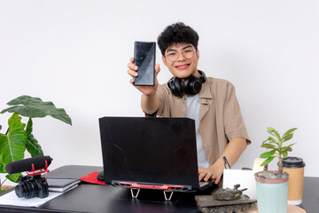 Cheerful freelance graphic designer at a modern workstation with a gaming laptop, holding up a...