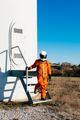 Man in space suit walking along metal stair of white futuristic structure in field