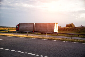 Obraz premium A truck with a semi-trailer and a hitch transports cargo against the backdrop of a field along the highway. Bulk cargo transportation concept, logistics company and business. Copy space for text