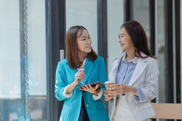 Obraz premium Happy two asian businesswoman working with tablet in meeting room, Businesswoman standing and talking about ideas in office workplace.
