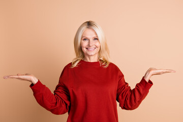 Photo of positive cheerful woman wear red sweater comparing arms empty space isolated beige color background