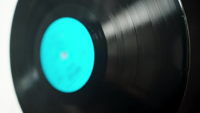 Vinyl record with a blue label rotating on a black-and-white background, selective focus.