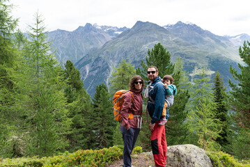 Fototapeta na wymiar Portrait of a smiling family with their little daughter in a baby carrier at father's back during a hiking day in Sölden, Austrian Alps.