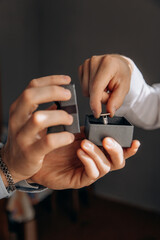 A close-up photo of a man taking a cufflink from a box. A friend helps to dress