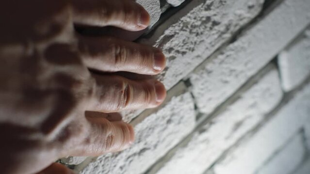 A man's hand touching a wall with a facing light brick, close-up