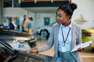 Young black saleswoman working at car dealership. - obrazy, fototapety, plakaty