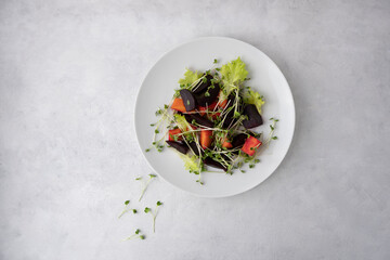 A healthy salad made from boiled beets, carrots, micro greens and lettuce. Dish on a light gray background and a white plate with olive oil and microgreens. Fresh tasty dish for healthy eating