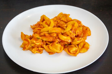 Traditional stuffed capeletti pasta with tomato sauce served on a white plate.
