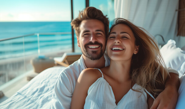 Young Beautiful Couple Radiates Joyful Happiness Together on Luxurious Hotel Room Bed with Breathtaking Sea View - Travel, Romance, and Relationship Goals in a Coastal Paradise