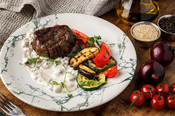 Grilled beef steak with vegetables on a white plate on a wooden background