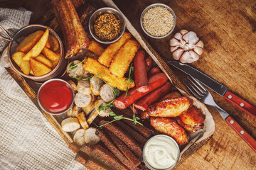 Grilled sausages with potatoes, cheese sticks, ribs and sauces on wooden background