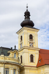 Fototapeta na wymiar The Holy Trinity Roman Catholic Church in Sibiu, Romania against the cloudy sky. A church bell tower in the old city center, in Transylvania