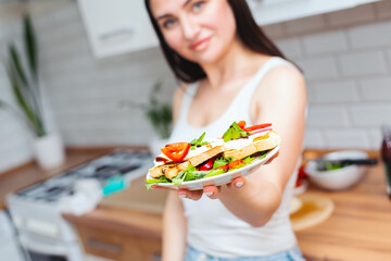 Beautiful woman in a white T-shirt and blue jeans holds a healthy breakfast of toast with arugula, cherry tomato and mozzarella cheese on a plate - 719237991