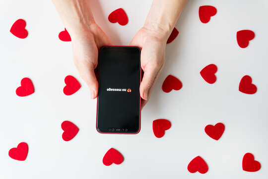 Two hands hold a smartphone with red hearts on a white background with the inscription no messages and a broken heart emoji.