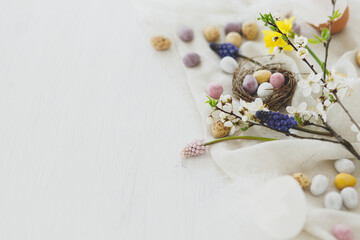 Happy Easter! Stylish easter chocolate eggs in nest, spring flowers, feathers and linen cloth on...