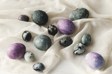 Stylish easter eggs and linen cloth on rustic white table. Space for text. Happy Easter! Natural painted marble and purple eggs. Seasons greetings