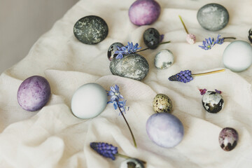 Happy Easter! Stylish easter eggs and spring flowers on linen cloth on rustic white table. Easter modern simple banner, space for text. Natural painted marble and purple eggs still life