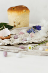 Fototapeta na wymiar Colorful easter chocolate eggs, easter bread, spring flowers and linen cloth on rustic wooden table. Easter modern simple decoration and homemade traditional cake. Happy Easter!