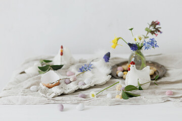Stylish easter chocolate eggs, spring flowers, chicken figurines and linen cloth on rustic wooden table. Space for text. Easter modern simple decoration. Happy Easter!